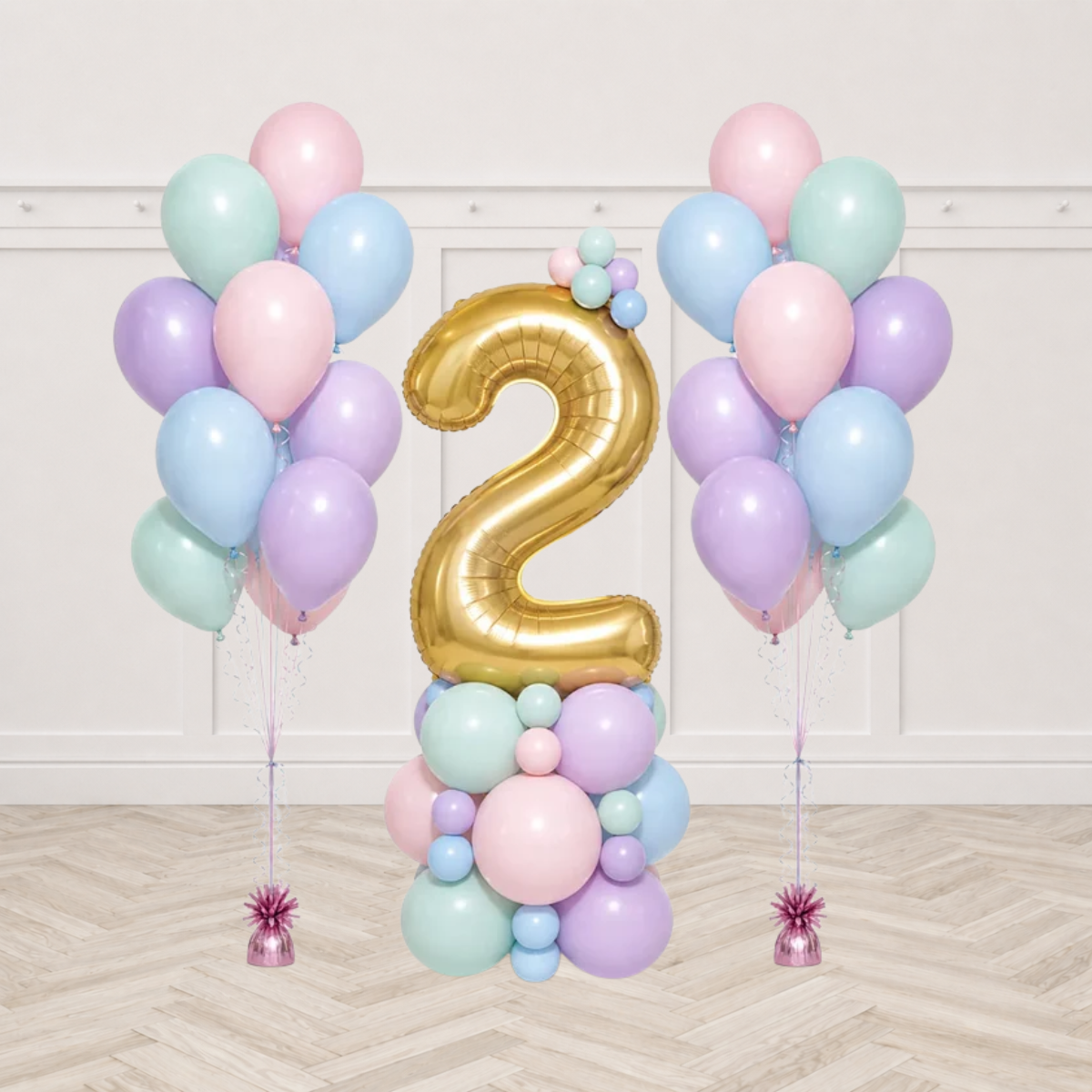 Two bunches of pastel pink mint blue and lilac latex balloons on pink weights beside a pastel balloon table top display with a gold number 2 foil balloon