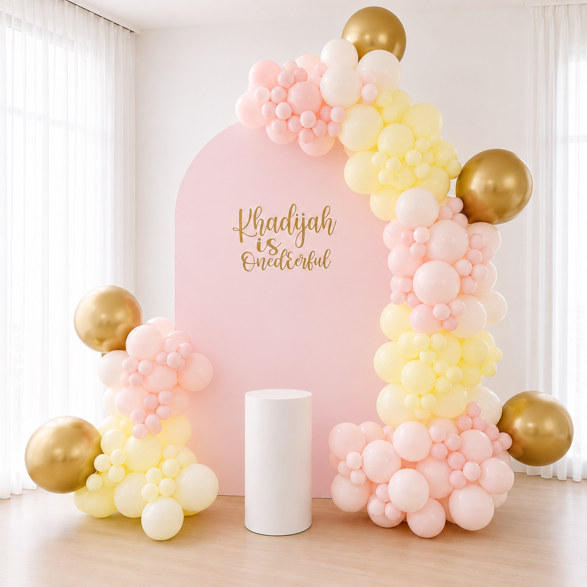 Blush pink, lemon and chrome gold balloon garland on a pink arch with a cake plinth